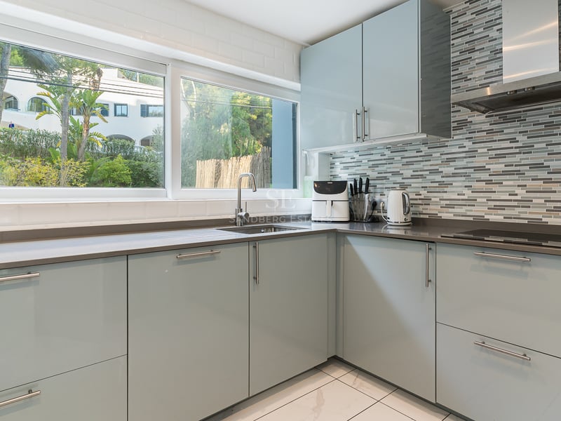 Cuisine moderne avec meubles bleu clair, plans de travail gris, grande fenêtre et crédence en mosaïque.