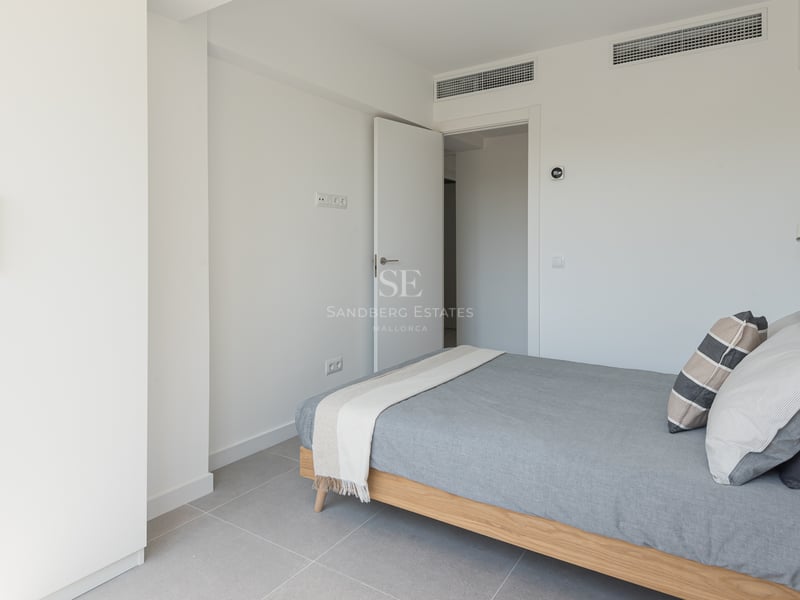 Chambre lumineuse avec cadre de lit en chêne, placards blancs et sol en grès gris dans une villa contemporaine.