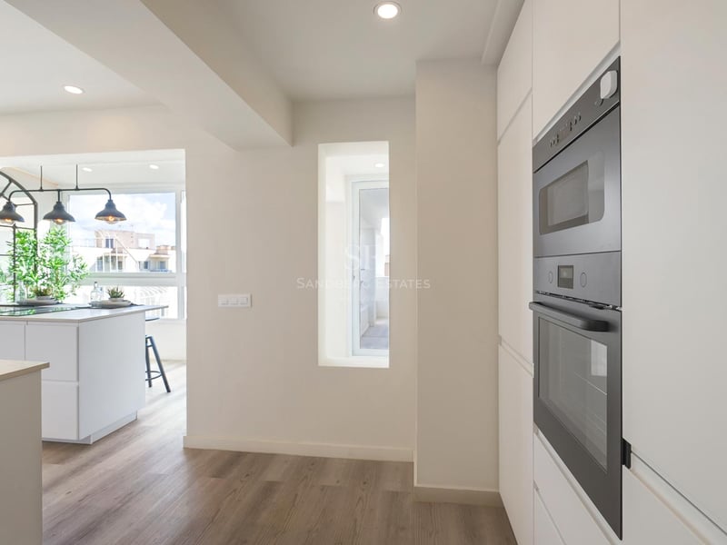 Moderne weiße Küche mit schwarzen Einbaubacköfen, Holzboden und weißer Insel unter Industrie-Leuchten.