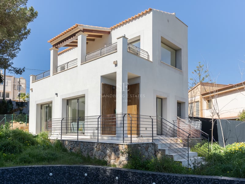 Vit modern tvåvåningsvilla med naturstenssockel och takpannor under en klarblå himmel.