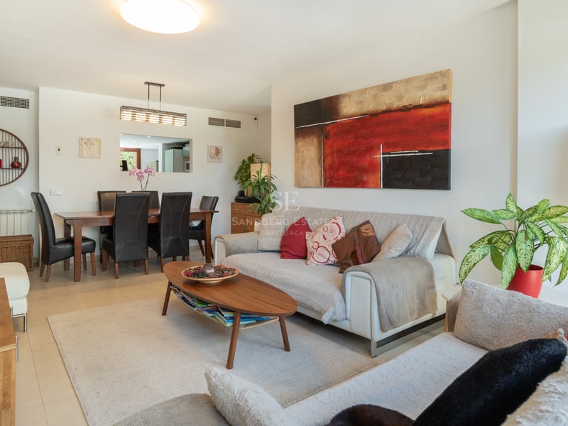 Salon lumineux avec canapés blancs, table basse en bois et coin repas avec chaises en cuir noir.