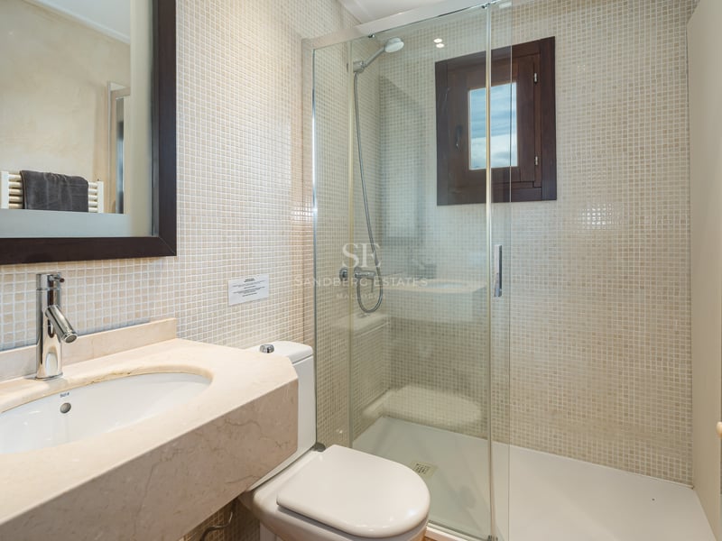 Salle de bain avec douche vitrée, murs en mosaïque beige et plan de toilette en marbre.