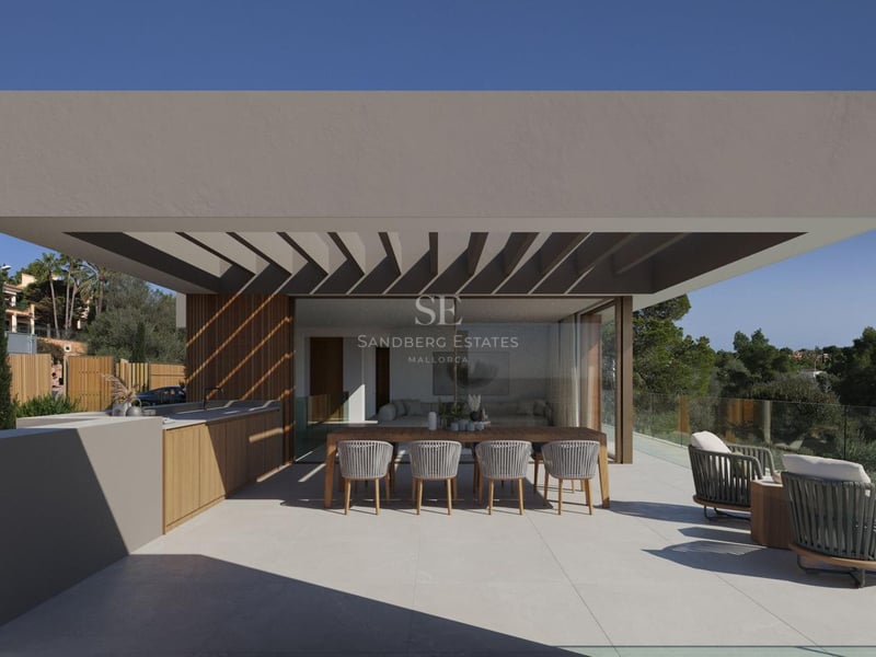 Terrasse ensoleillée avec cuisine extérieure, table en bois et fauteuils lounge face à une pinède.