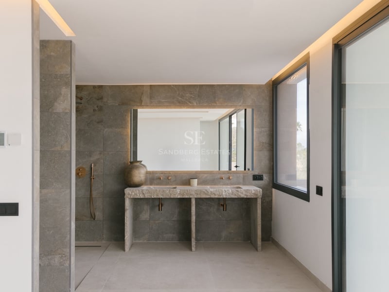 Modernes Badezimmer mit Doppelwaschtisch aus Stein, hinterleuchtetem Spiegel und Messingarmaturen.