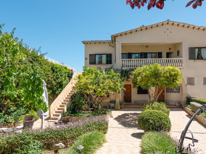 Exteriör av en medelhavsvilla i två våningar med gröna fönsterluckor, stentappa och en anlagd innergård.