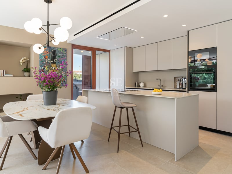 Modern kitchen featuring a cream island, marble dining table with white chairs, and contemporary pendant lighting.