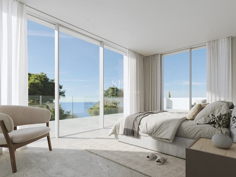 Chambre principale minimaliste dotée de baies vitrées du sol au plafond s'ouvrant sur une terrasse en pierre avec vue mer.