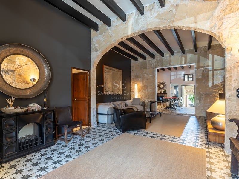 Vue intérieure d'un salon avec une arche en pierre naturelle, des poutres foncées et des carreaux de ciment géométriques.