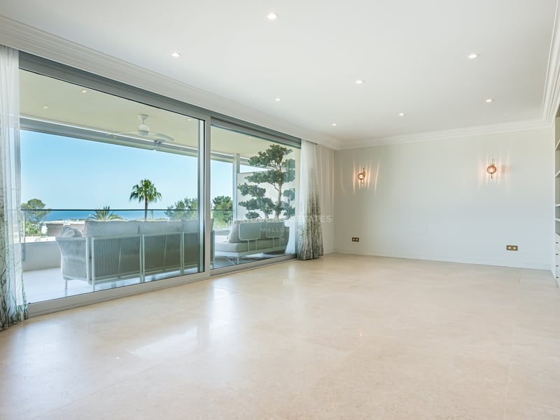 An empty luxury living room with marble floors and large glass doors opening to a terrace with sea views.