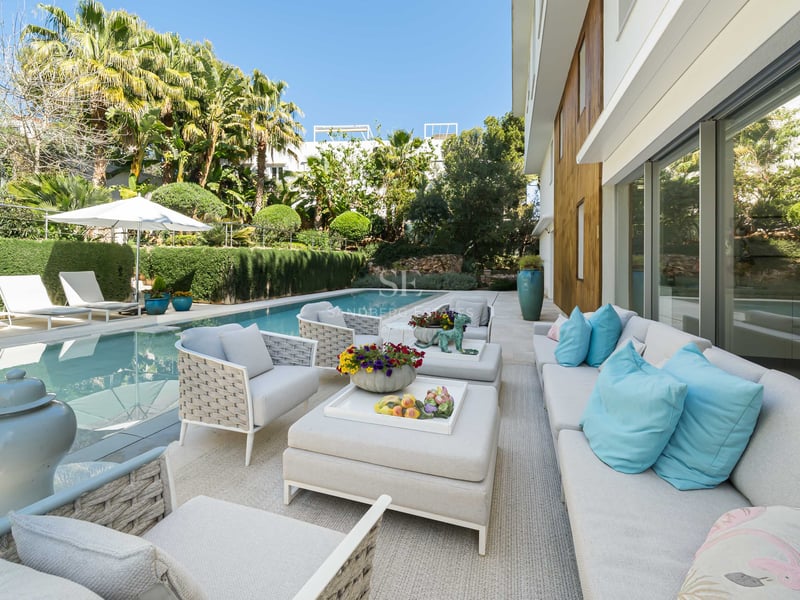 Moderne Außenterrasse mit weißen Loungemöbeln, türkisfarbenen Kissen, Pool und üppigem mediterranem Garten.