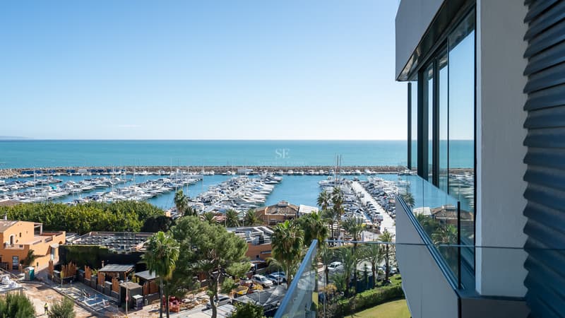 Upphöjd vy från en modern balkong över en marina med yachter och Medelhavet under en klarblå himmel.
