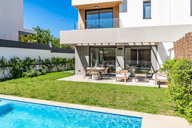 Villa contemporaine avec piscine turquoise, pelouse soignée et terrasse ombragée avec mobilier design.