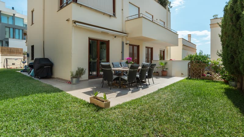 Patio extérieur avec table à manger et chaises sur une terrasse carrelée entourée d'une pelouse verte soignée.
