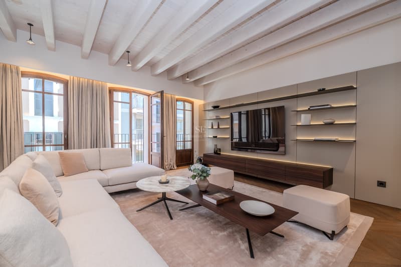 Salon spacieux avec plafond à poutres blanches, canapé d'angle crème et meuble TV rétroéclairé.