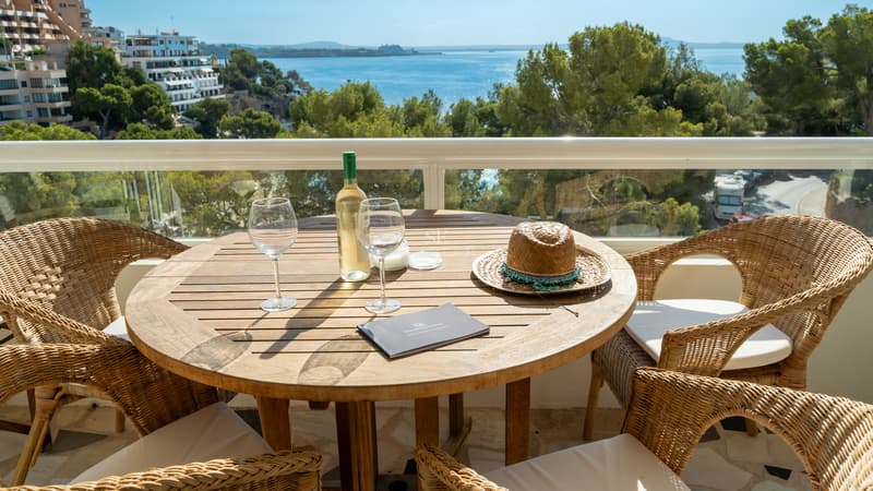 Erhöhte Terrasse mit Holztisch, Korbstühlen und weitem Blick über das Meer und Pinienwälder.