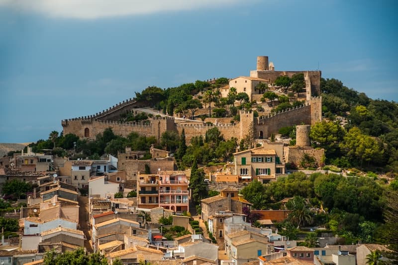 Village méditerranéen perché couronné par une forteresse médiévale avec des murs en pierre sous un ciel bleu.