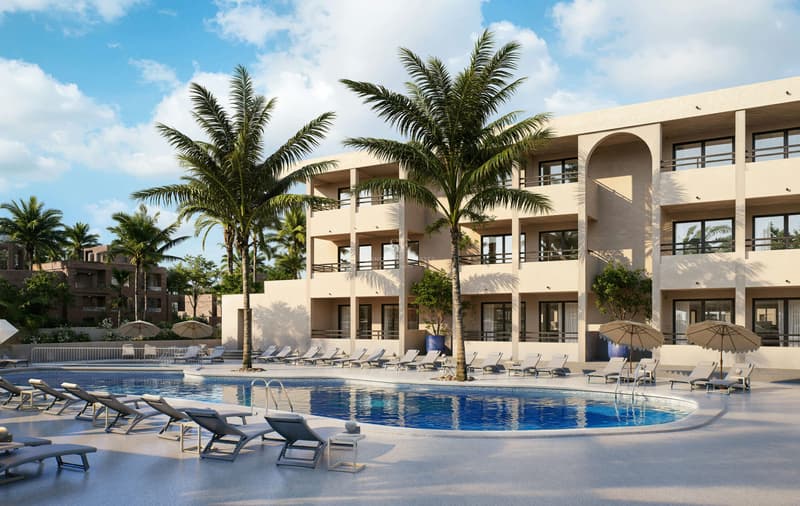 Grande piscine bleue avec chaises longues, palmiers et bâtiment méditerranéen moderne de trois étages sous un ciel clair.