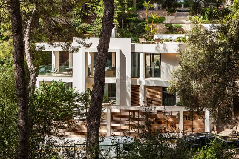 Mehrstöckige moderne Villa mit Steinfassade, Holzlamellen und Glasterrassen, umgeben von alten Pinien.