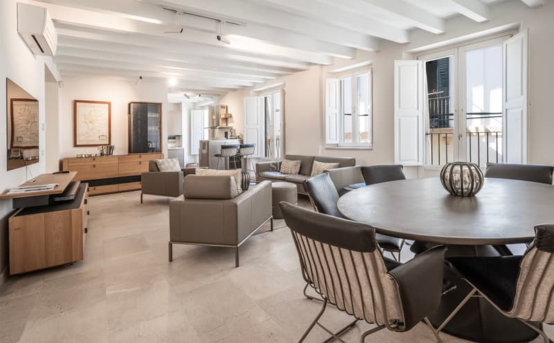 Geräumiges Wohnzimmer mit weißen Holzbalkendecken, grauen Ledermöbeln und rundem Esstisch.