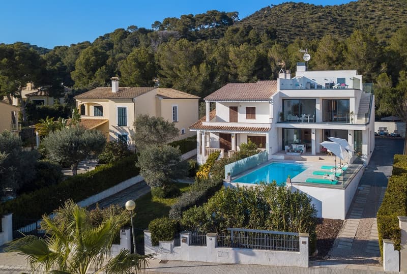 Vue aérienne d'une villa blanche contemporaine avec piscine, terrasses en verre et collines verdoyantes.