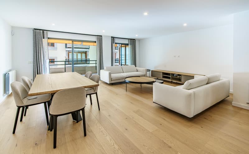 Séjour ouvert avec canapés blancs, table à manger en bois et grandes baies vitrées donnant sur un balcon.