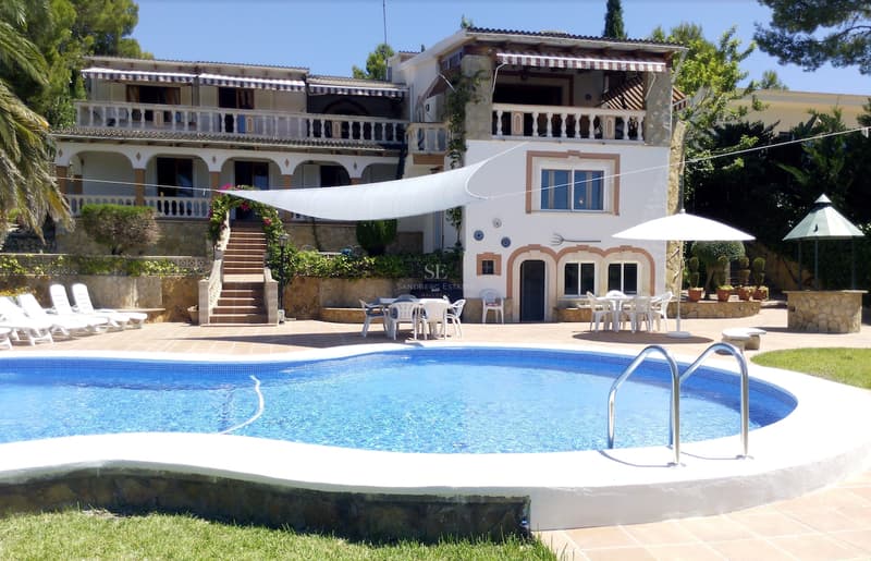 Grande piscine de forme libre avec terrasse en terre cuite et villa blanche traditionnelle à plusieurs niveaux.