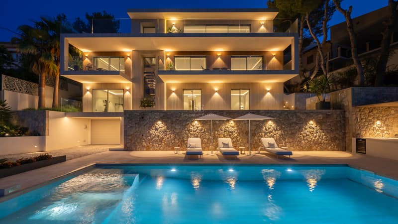 Vue nocturne d'une villa contemporaine à plusieurs niveaux avec piscine éclairée et chaises longues.