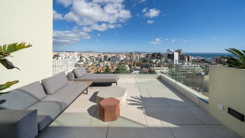 Toit-terrasse moderne avec canapés gris et garde-corps en verre offrant une vue sur la ville et la mer.