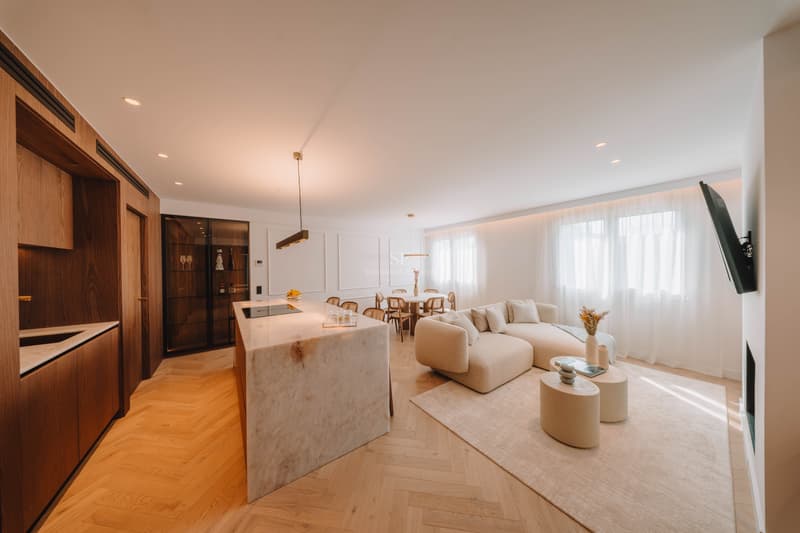 Offener Wohnbereich mit Marmorinsel, beige Sofa und Fischgrätparkett.