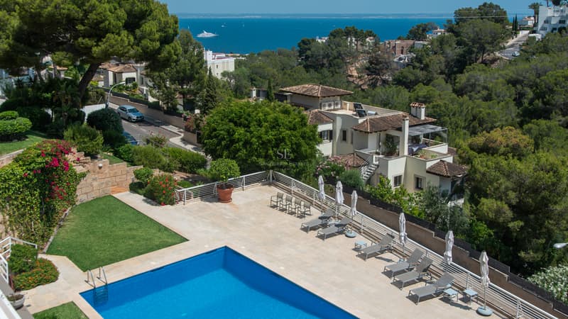 Aerial view of a blue swimming pool and sun deck overlooking the Mediterranean sea and coastal villas.