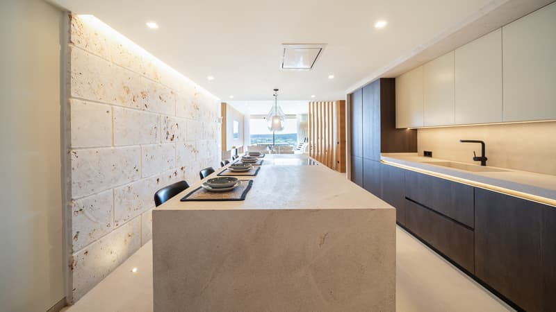 Cuisine contemporaine élégante avec un grand îlot en pierre, des armoires en bois sombre et un mur en pierre texturée.
