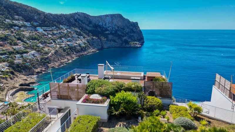 Modern rooftop terrace with glass railings overlooking a blue sea and rugged coastal cliffs.