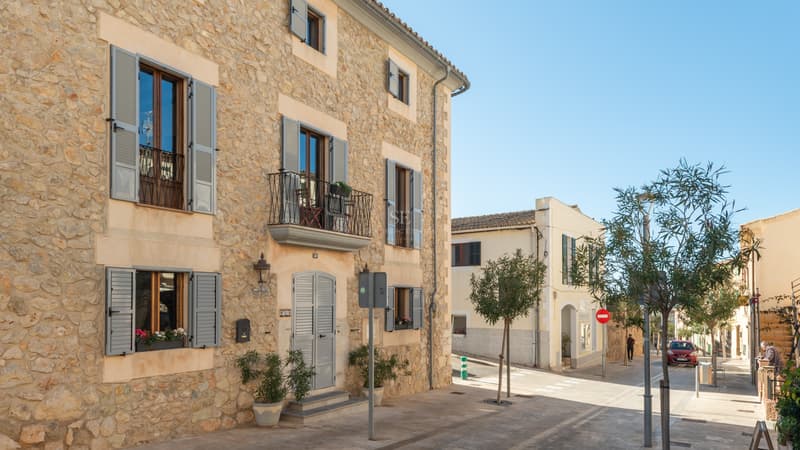 Immeuble en pierre traditionnelle avec volets gris et balcons en fer dans une rue ensoleillée.