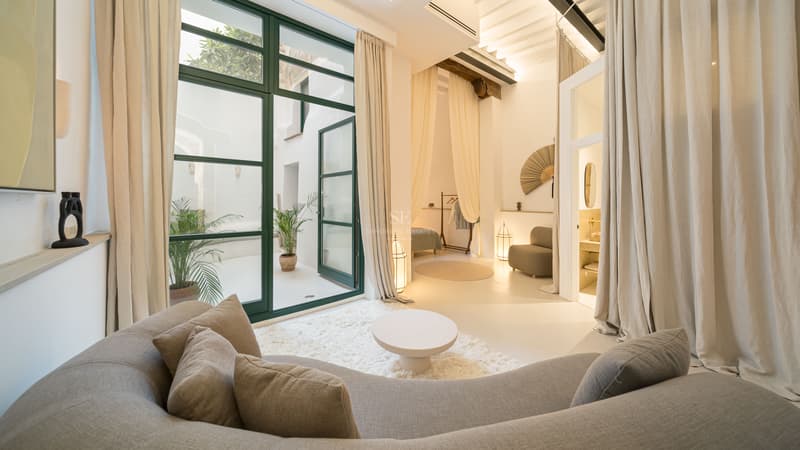 Modern living room with a large curved sofa, shaggy rug, and floor-to-ceiling glass doors opening to a white patio.