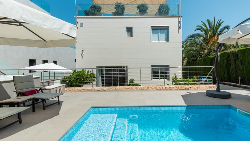 Piscine extérieure privée turquoise avec transats, parasols blancs et façade d'une villa moderne.