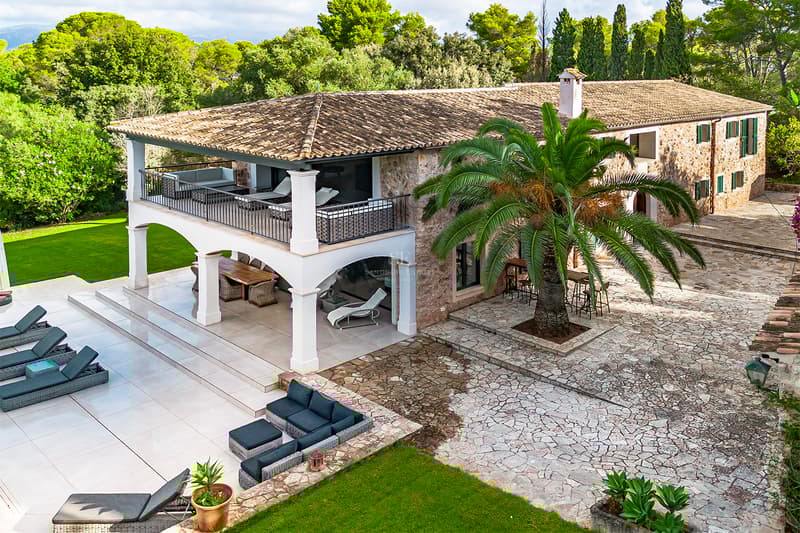 Vue aérienne d'une villa en pierre avec des arches blanches, des terrasses extérieures et un palmier mature.