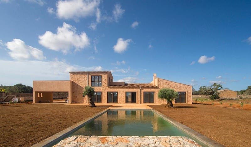 Vue extérieure d'une villa en pierre naturelle avec piscine rectangulaire et oliviers sous un ciel bleu.