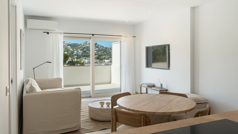 Modernt vardagsrum med möbler i ljust trä och stora glaspartier som leder ut till en terrass med utsikt.