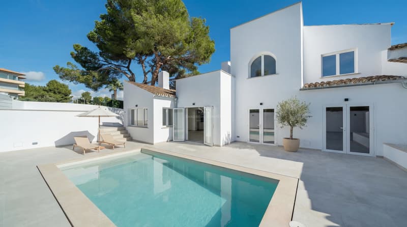 Modern white villa with a turquoise swimming pool, stone terrace, and sun loungers under a clear blue sky.
