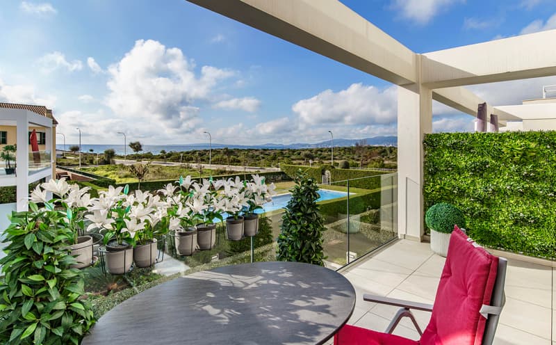 Luxus-Terrasse mit Tisch, rotem Stuhl und Glasgeländer mit Blick auf Garten, Pool und Meer.