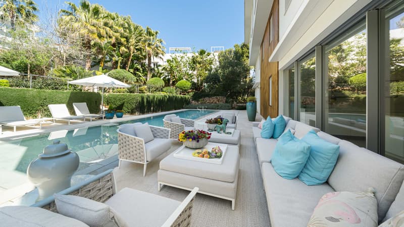 Moderne Außenterrasse mit weißen Loungemöbeln, türkisfarbenen Kissen, Pool und üppigem mediterranem Garten.