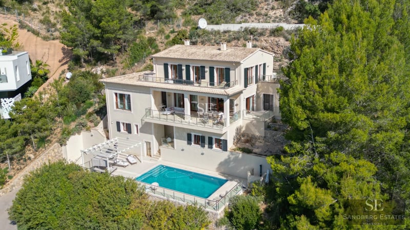 View of a luxurious infinity pool with sea views from a modern villa featuring large windows and a terrace.