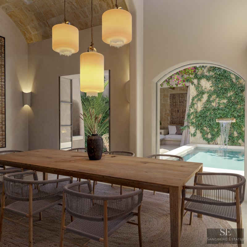 A large wooden dining table with woven chairs under three pendant lights, looking out to a courtyard plunge pool.