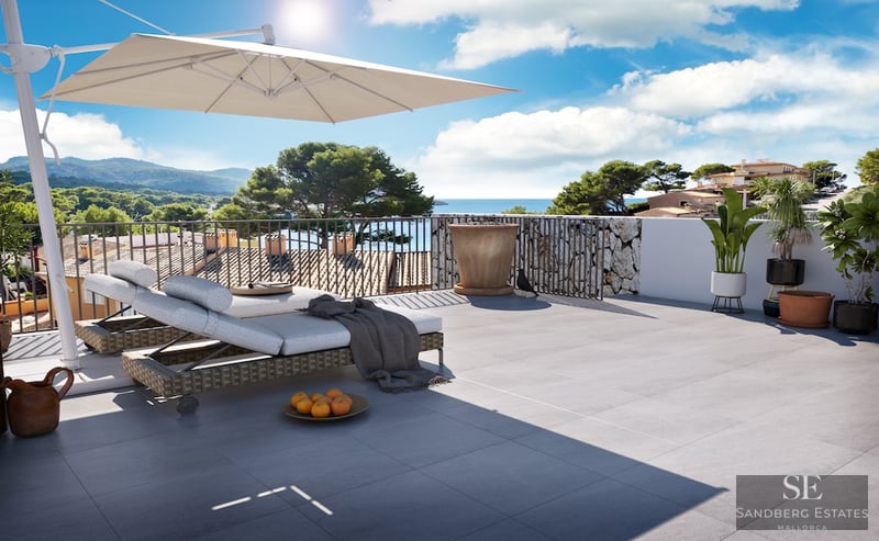 Sunny terrace with lounge chairs, large umbrella, and panoramic sea and mountain views.