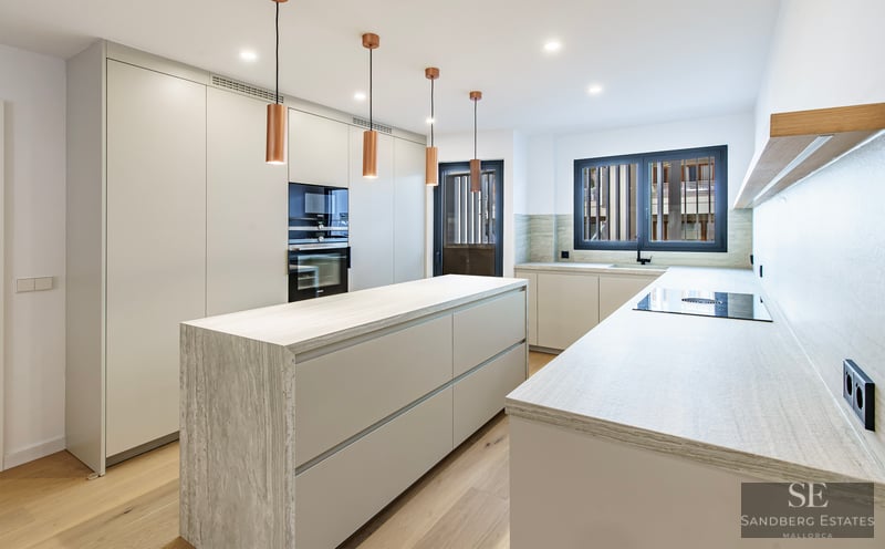 Modernt vitt kök med köksö i sten, pendellampor i koppar och trägolv.