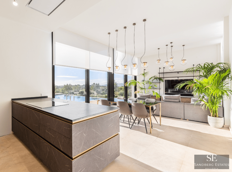 Offener Wohnbereich mit Kücheninsel aus Stein, Essplatz und großen Fenstern mit Blick auf den Pool.