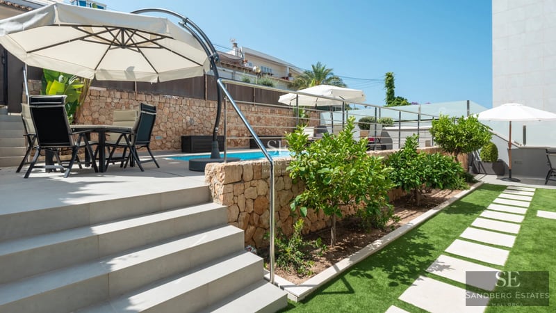 Spacious living room with floor-to-ceiling windows, light wood floors, modern fireplace, and garden views. Minimalist design with warm touches.
