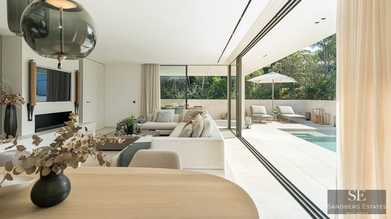 Modern bright living room with large glass doors opening to a sunlit terrace and private swimming pool.
