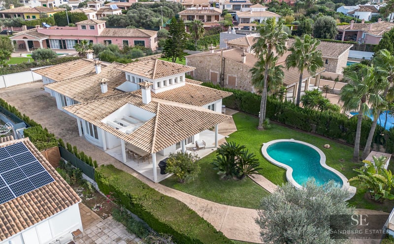 Aerial view of a white villa with a terracotta roof, a turquoise swimming pool, and a lush green garden.