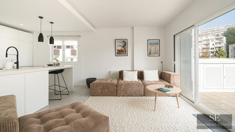 Bright living room with brown corduroy modular sofa, white textured rug, kitchen island, and large glass doors to a balcony.